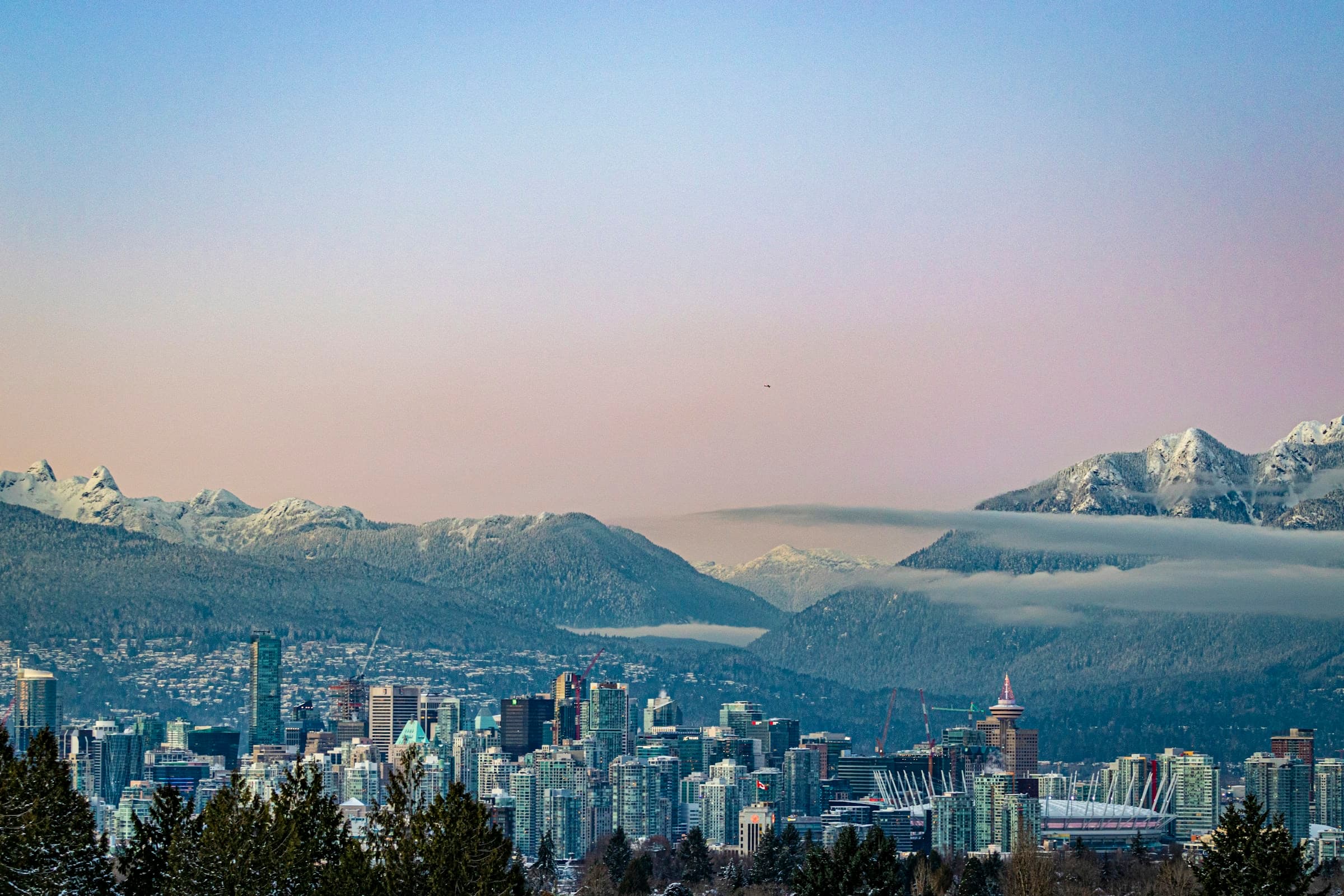 Downtown Vancouver below snow-covered mountains at dusk