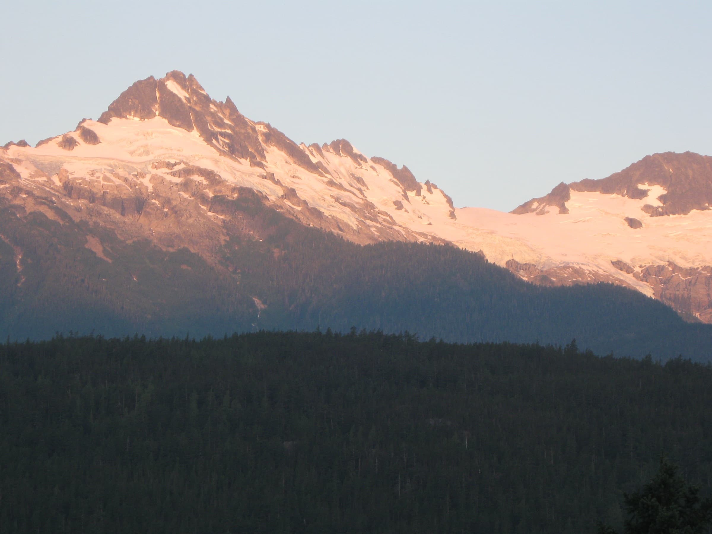 First light on the Tantalus Range above dark forest, seen from the Sea to Sky Highway